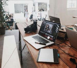 A bright, modern workspace featuring laptops, a camera, and a drawing tablet in an indoor office.